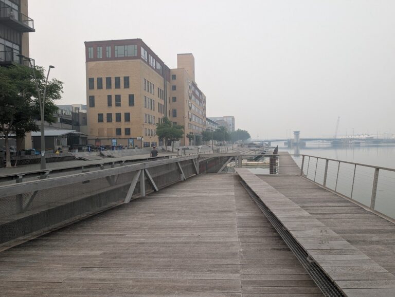 A broad CityDeck boardwalk beside downtown buildings and the Fox River.