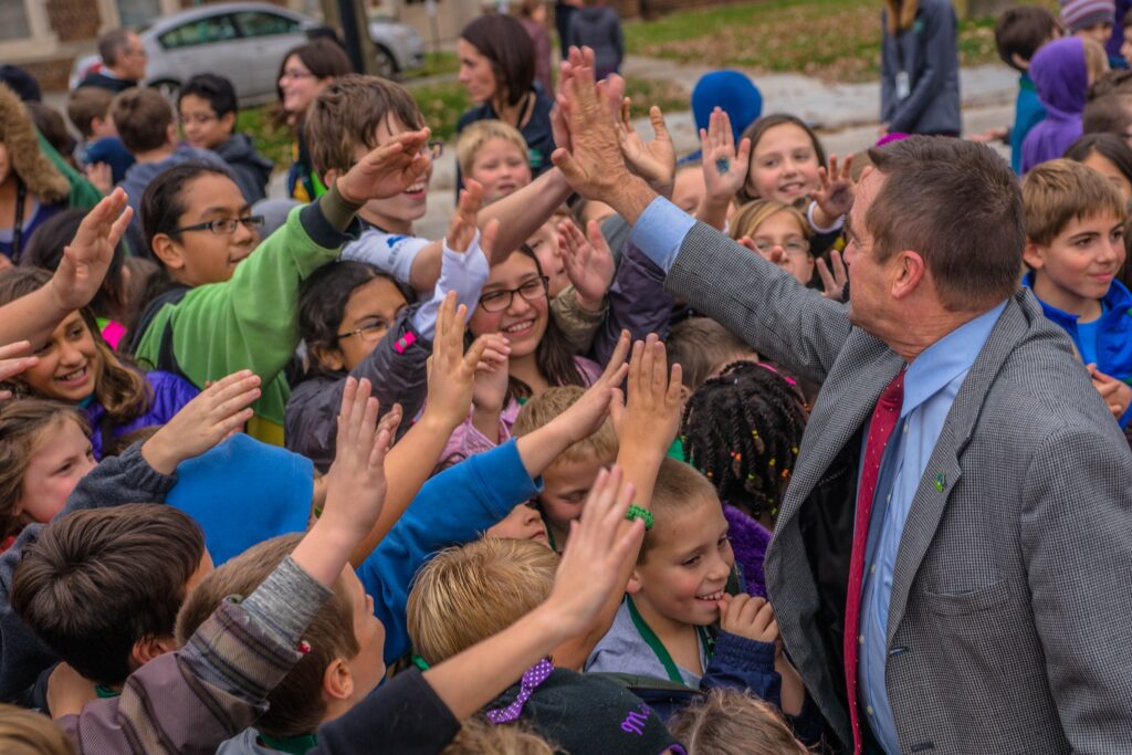 Jim Schmitt greeting a large group of Green Bay students outdoors.