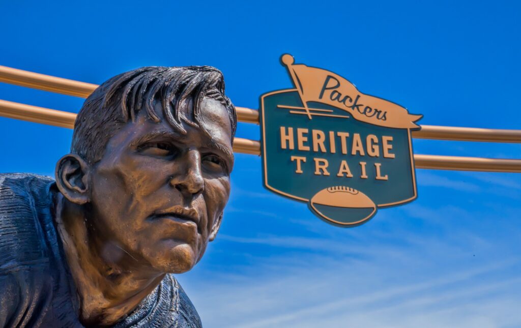 A Packers Heritage Trail bronze statue beneath the trail sign.
