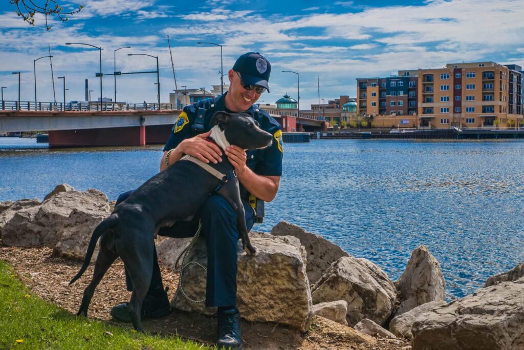 A Green Bay police officer sitting with a police dog beside the Fox River.