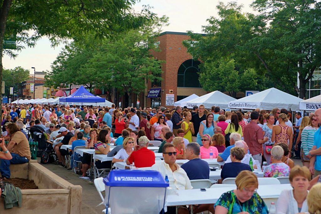 A large outdoor neighborhood gathering with residents seated at community tables.