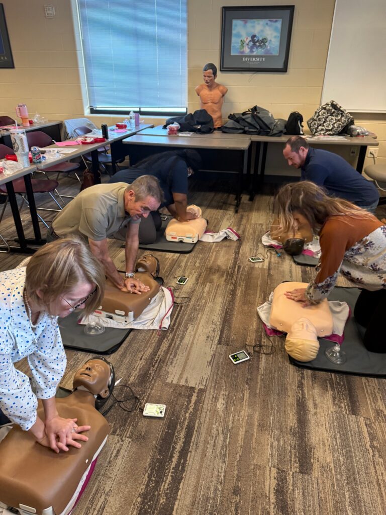 Jim practices chest compressions on a training mannequin alongside other participants in a classroom.